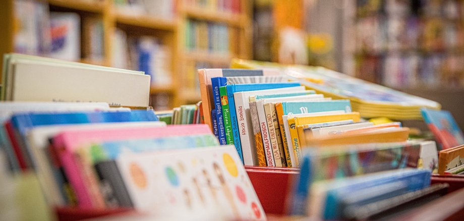 Bücherei Bunte Kinderbücher stehen in roten Kisten aufgereiht in einer Bücherei oder Buchhandlung. Im Hintergrund sind Bücherregale mit weiteren Büchern zu sehen.