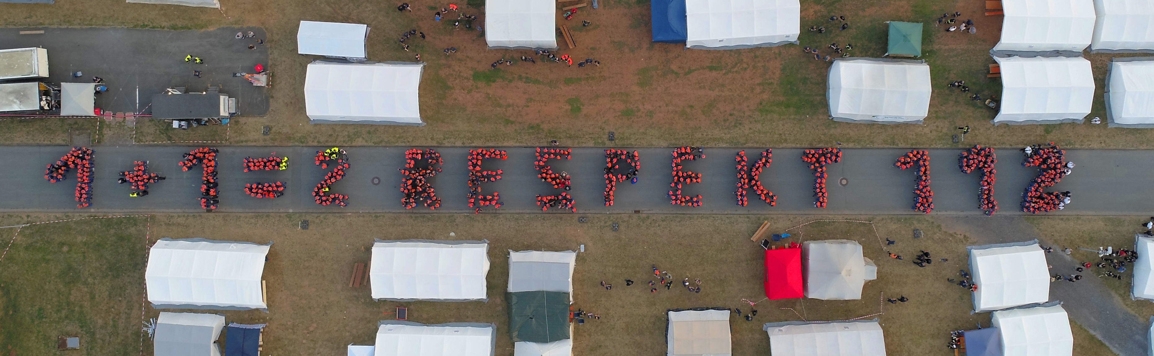 Personen formen den Schriftzug 1 plus 1 gleich 2 Respekt 112 Luftaufnahme