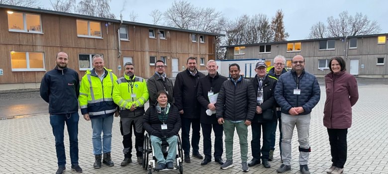 Die Mitglieder der Integrationskommission stehen aufgereiht nebeneinander in einem Innenhof. Es sind zehn Männer und zwei Frauen. Eine der Frauen sitzt im Rollstuhl.