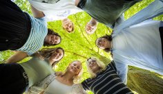 Zusammenstehen Jüngere Personen stehen im Kreis und blicken nach unten in die Kamera