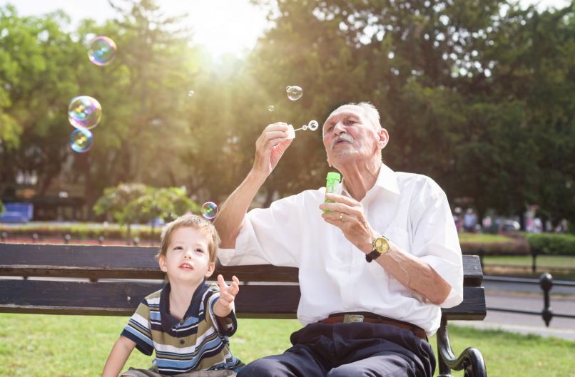 Enkel und Großvater mit Seifenblasen auf einer Parkbank